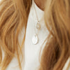 Två smycken ur ZOE HOOPS kollektion på en kvinna med vit tröja och långt blont hår