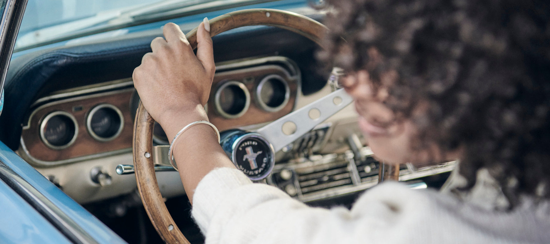 Kvinna som kör en fin vintagebil och har ett smycke på handleden