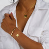 Kvinna med halsband och två armband i guld och vit skjorta