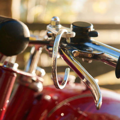 Ett armband i silver hänger på styret till en röd klassisk motorcykel, mycket trendig och häftig bild