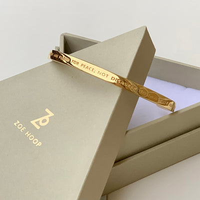 Armband i guld med inskription, kreativt lagt på en smyckesask från ZOE HOOP