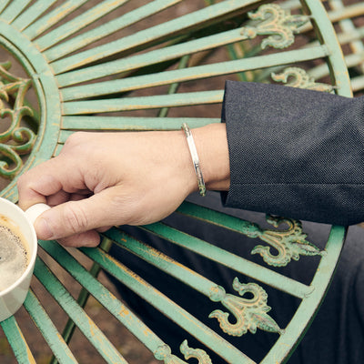 Manlig hand med armband håller en kaffekopp på ett rustikt cafebord
