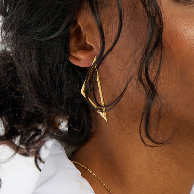 Inzoomat trekantigt statement örhänge i guld på kvinna med mörkt hår och vit skjorta